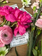 Flat lay of peonies and ranunculus styled for a bridal shower, Madison's Meadow branded tags